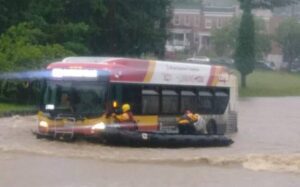 Photo of people on a flooded street in a raft next to a bus