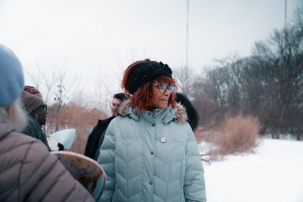 Felice Green is standing in the middle with her head towards her left. The background is snow and there are other people pictured.