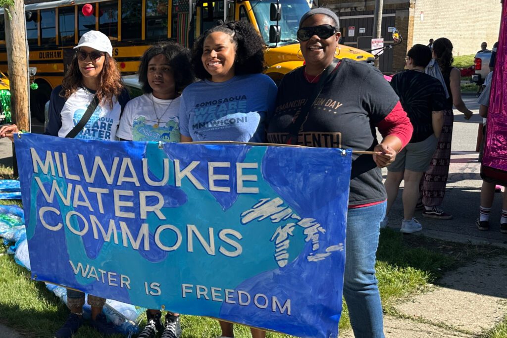 Felice and family holds a blue painted sign reading "Milwaukee Water Commons Water is Freedom"